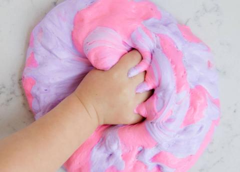 Picture of a kid's hand grabbing fluffy pink and blue slime. 