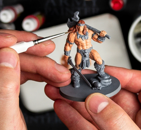 An image of someone painting miniature model of a fantasy barbarian figure.
