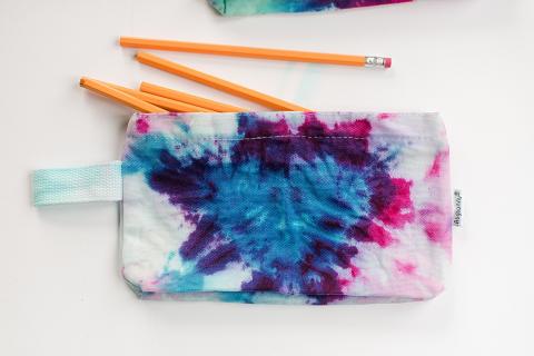 Picture of a white canvas pencil case with pink, blue and purple tie dye. 