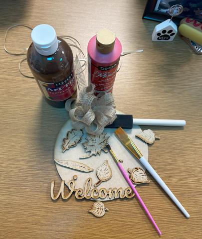 Wooden sign with leaves and the word welcome, paint, and paint brushes