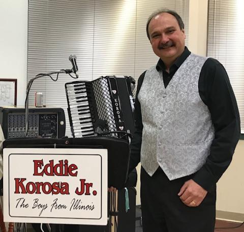 Eddie Korosa next to an accordian and a sign with his band name