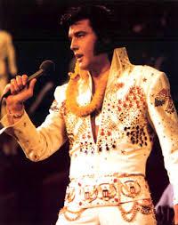 Elvis Presley wearing a white jeweled suit singing into a microophone
