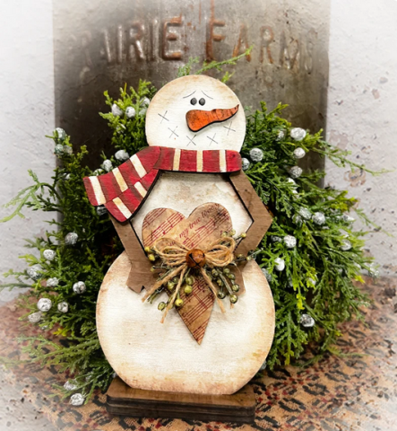 Snowman with red and brown scarf holding a heart with a bell and twine