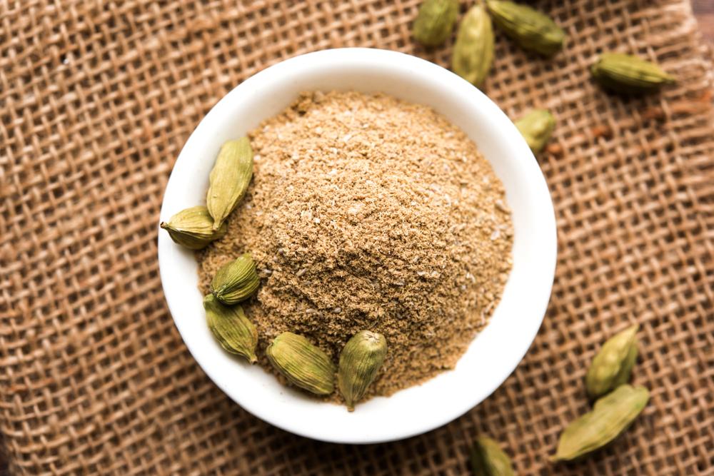 White bowl with cardamom powder and pods