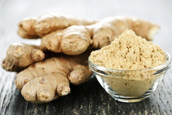 Ginger root in a small glass bowl and multiple ginger roots behind the bowl